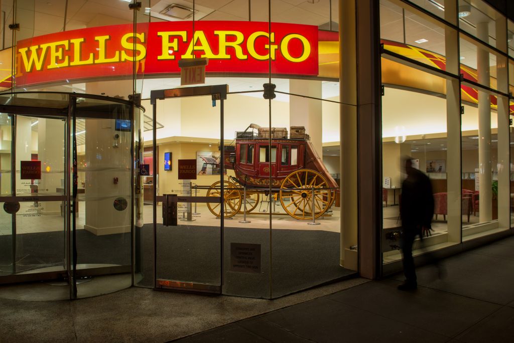 A pedestrian walks past a Wells Fargo & Co. bank branch at night in New York, U.S., on Saturday, April 11, 2015. Wells Fargo & Co. is scheduled to release earnings figures on April 14. Photographer: Craig Warga/Bloomberg via Getty Images